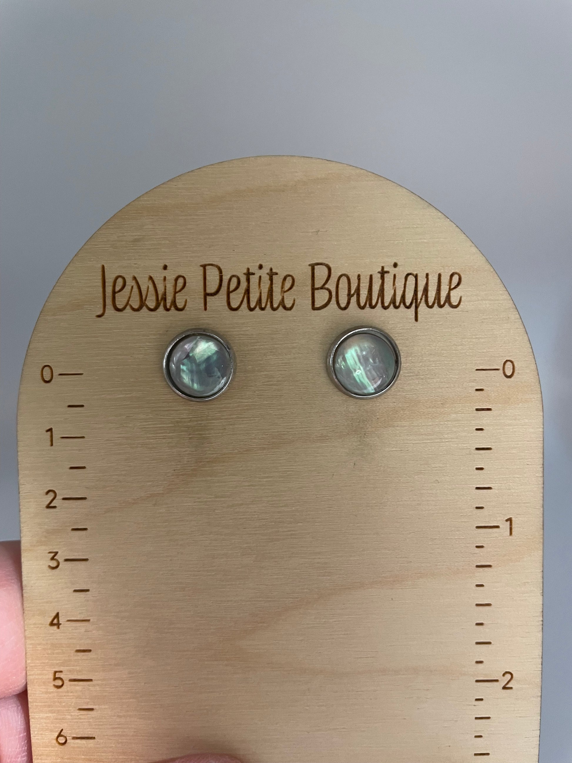 Wooden measuring tool with 'Jessie Petite Boutique' branding and two earrings on a light gray background.