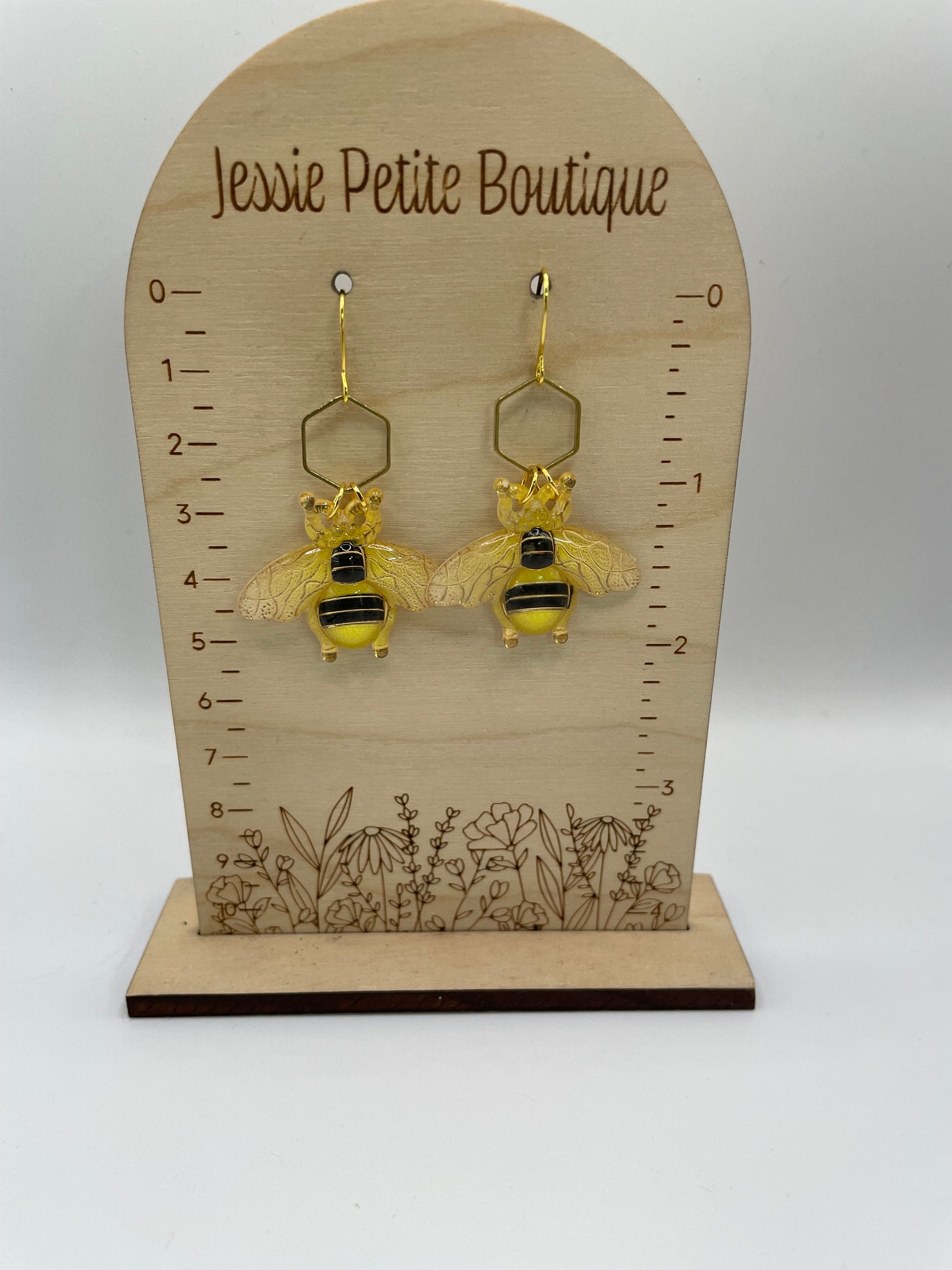 Bee-themed earrings on a wooden display card with measurement scale and floral design.